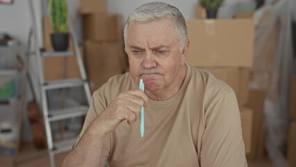 Man sitting holding pen to chin among packed cardboard boxes and a ladder in a building during a move; pensive planning.