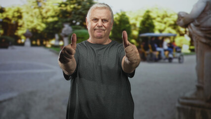 Man standing with arms at sides, wearing gray t shirt on a city street beside statue and trees; calm reflection.