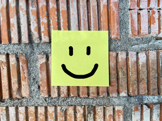 Smiley face note attached to brick wall, symbolizing positivity, happiness, simple joy, and mental wellness concept.
