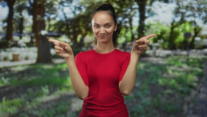 Young hispanic woman clasping hands then blows a kiss with a smile in a sunlit forest setting; affection connection.