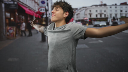 Fototapeta premium Teenage boy with outstretched bare arms smiling and looking sideways on a city street; joy openness youthful confidence.