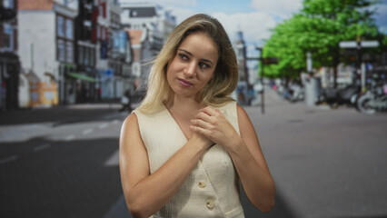 Woman clasping hands to chest on a busy city street with closed eyes and gentle tilt of head, wearing sleeveless vest; serenity.