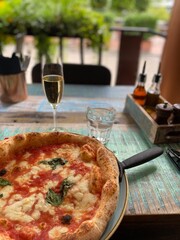 Margherita Pizza with Wine at Outdoor Restaurant Table; Italian Pizza and Wine Served at Cozy Outdoor Bistro; freshly baked margherita pizza with tomato sauce, melted cheese, and basil