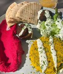Middle Eastern Mezze Plate with Falafel, Hummus and Pita Bread; Colorful Vegan Mezze Dish with Falafel, Couscous and Fresh Salad; falafel with tahini sauce, hummus, couscous, fresh salad, and pita 