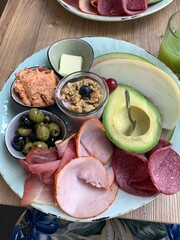 Breakfast Plate with Cold Cuts, Avocado, Yogurt and Fresh Sides; Healthy Brunch Plate with Avocado, Charcuterie and Yogurt; cold cuts, avocado, yogurt with granola, olives, butter, melon, and spreads