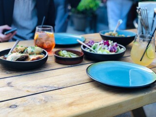 Traditional Danish Bistro Table with Shared Nordic Food and Drinks; Scandinavian Bistro Dining; fresh salad, roasted meat, potatoes, pickles, and refreshing drinks on a rustic wooden table