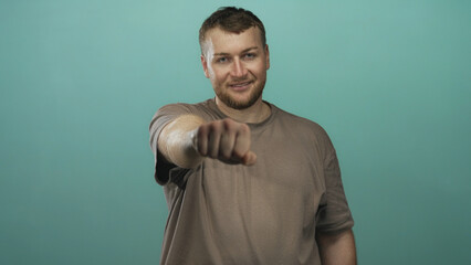 Man pointing fist toward camera in teal studio with visible forearm and casual tshirt; confidence greeting.