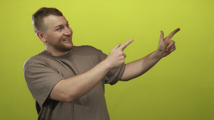 Man pointing with both hands and fingers in green studio while smiling and directing attention to the right; playful energy.