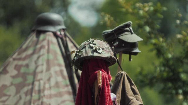 Arrangement of German military helmets and caps, including a camouflaged Stahlhelm with foliage and a M43 field cap. Historical conflict era equipment and WWII war history reenactment props.