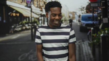 Man pointing finger upward with his right hand on a busy city street wearing a striped t shirt and smiling broadly; optimism inspiration motivation confidence.