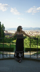 Naklejka premium Woman standing with arms outstretched on viewpoint railing in florence wearing black sundress and sunglasses, bare feet visible; serenity.