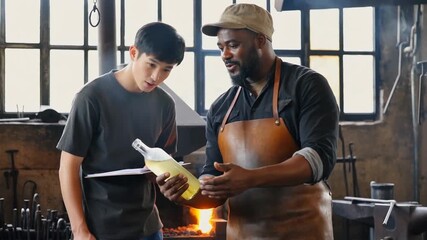 Two men working together in an artisan workshop, discussing techniques while holding a glass bottle with a vibrant yellow liquid