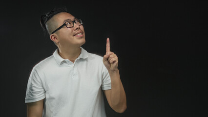 Man pointing index finger upward in black studio backdrop wearing white polo; curiosity idea insight.