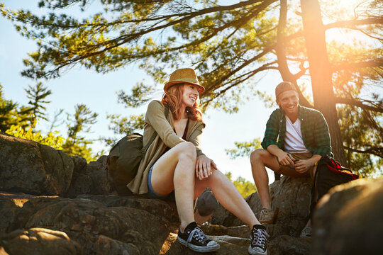 Couple, hiking and relax in woods for vacation, funny joke or break on adventure together in nature. Rest, man and woman trekking in forest for holiday, sightseeing and laugh with happy partner