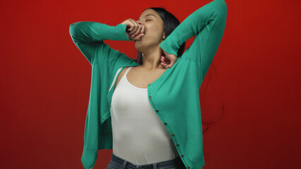 Woman stretching arms above head with closed eyes in red studio wearing green cardigan and white tank; serenity.