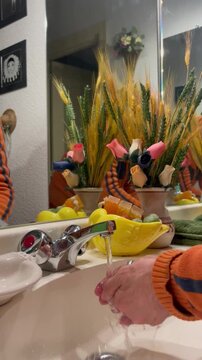 Lavando manos con agua y jab&oacute;n en lavabo de ba&ntilde;o de casa con espejo y colorido