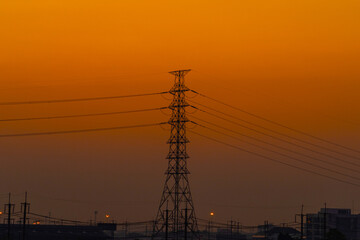 Silhouette of a high voltage transmission tower orange sunset sky. concept Industrial energy infrastructure and power lines