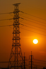 Silhouette of a high voltage transmission tower orange sunset sky. concept Industrial energy infrastructure and power lines