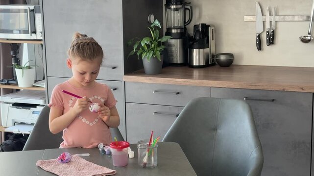 Child smiling while painting Easter eggs at the table. Joyful participation in seasonal family traditions.