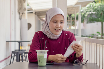 A young Indonesian Muslim woman shocked while looking at her shopping receipt
