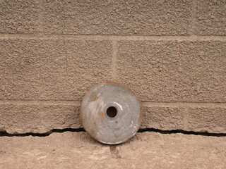 Old abrasive grinding wheel leaning against cracked concrete wall near ground.