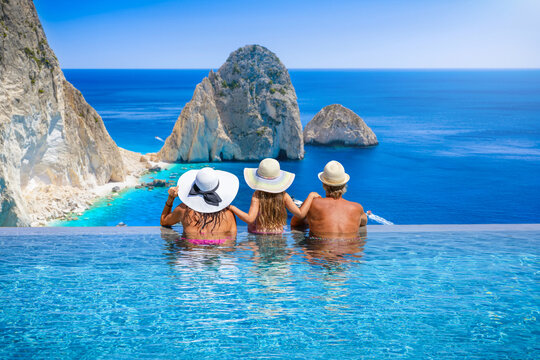 A family in a swimming pool enjoys the infinity view of the Mizithres rocks and beaches on Zakynthos island, Ionian Sea, Greece, during their summer holidays