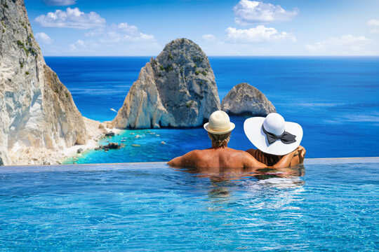 A couple swimming in an infinity pool and enjoying the view of the famous Mizithres rocks and beaches at Zakynthos island, Greece, during summer vacation time