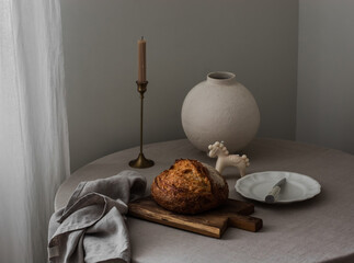 Sourdough bread, a candle, a vase, a plate on a round table with a gray tablecloth in the living room