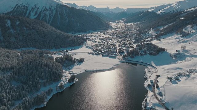 Cinematic Aerial Winter View of Davos Switzerland With Snow Covered Alpine City, Frozen Lake and Mountain Valley Symbolizing Global Meetings, Luxury Travel, Climate Dialogue, Serenity and High Altitud