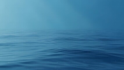 Deep blue ocean water surface with gentle ripples under a clear hazy sky.