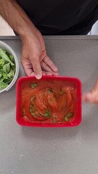 San Marzano tomato pizza sauce preparation mixing fresh basil leaves olive oil and salt in bowl from above vertical video