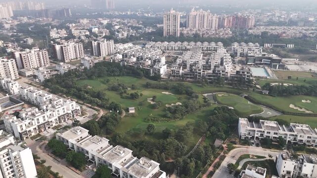 Aerial footage showcasing a lush golf course surrounded by luxury residences and high-rise towers under light NCR haze. Expanding townships of Greater Noida create strong urban visuals
