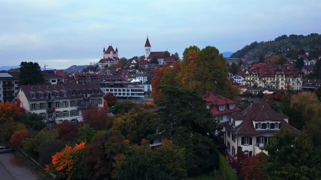 Thun Castle Flusswelle Aare River Schloss Thun Thunersee Switzerland Schweiz Europe aerial drone Autumn Fall morning grey skies buildings yellow birches tree Bernese Oberland upwards jib motion