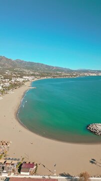 Vertical aerial pan of Puerto Ban&uacute;s beach, Marbella, Southern Spain, sunny day, turquoise water, with La Concha mountain in the background.