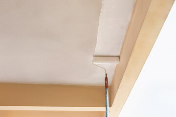 Painter using a roller to apply fresh white paint to a ceiling.