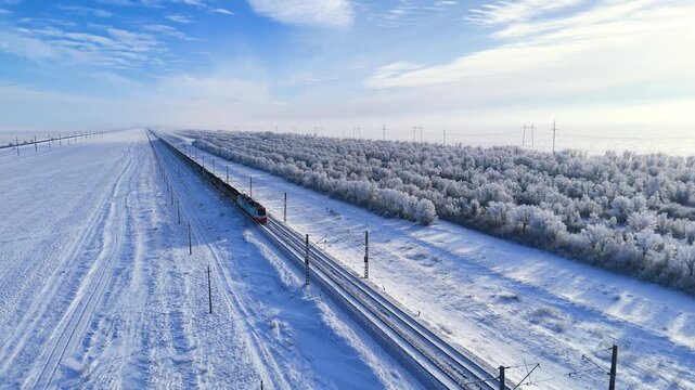 A train is traveling on a winter railway, and the trees are covered in white frost.