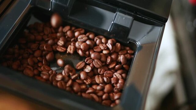 Close-up of coffee beans being poured into the coffee machine hopper Concept of coffee preparation, freshness, aroma, barista routine, home brewing and coffee culture. 