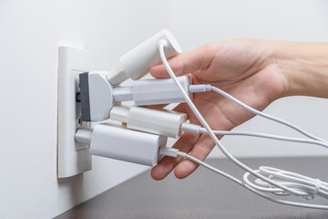 Hand inserting electrical plugs into outlet. Electrical overload