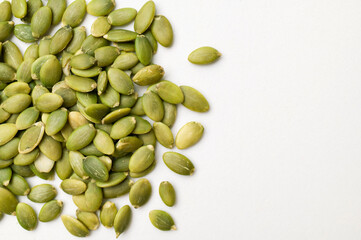 Scattered green fresh pumpkin seeds on light gray background, top view. Organic, healthy pumpkin seeds, rich in vitamins, minerals and fiber. Healthy food background