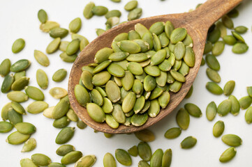 Raw peeled green pumpkin seeds in wooden spoon on light gray white background top view. Food background, Organic healthy tasty pumpkin seeds, Autumn cooking ingredient. Plant-based protein source