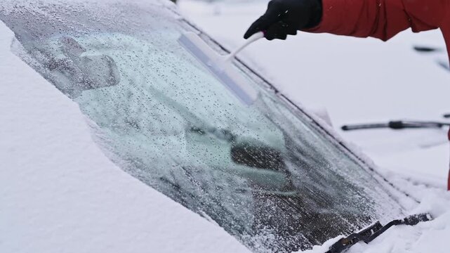 male hand in glove clean ice  from car's windshield with scraper car parked on residential street cold morning. Close-up no face