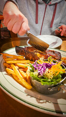 Cutting with knife into a delicious roasted grilled rack of beef of pork BBQ ribs served with fries and a fresh side salad on plate at restaurant as tasty main dish for delicious lunch or dinner