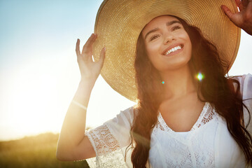 Fototapeta premium Thinking, woman and smile with hat in nature for travel, fresh air and reflection on holiday. Space, female person and vacation with vision in field, daydreaming and sightseeing view in countryside