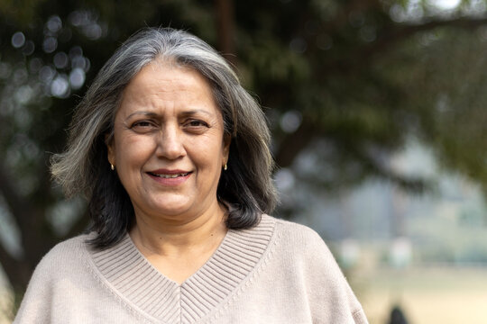 Close shot of a happy indian elder woman fun at park. Portrait of a cute, attractive, blonde, lovely, elegant and beautiful senior woman spending leisure time at outdoors background nature, copy space