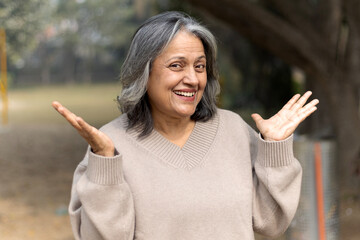 Indian happy senior woman spread her arms in environment nature like the wings of a bird. Happiness. Freedom. Elderly woman stands with one hand open in a park. Indian active old age at woman in park © Pix4Ads