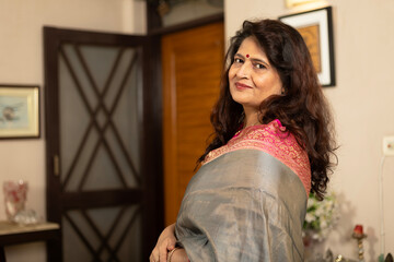 Fototapeta premium Portrait of a indian happy matured or senior woman smiling while relaxing. sitting on sofa at home looking at camera