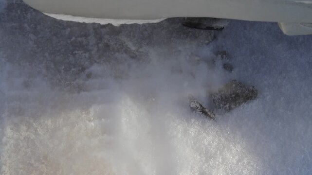 Snow piles up around the exhaust pipe of a parked car during winter. Cold air creates a cloud of exhaust as the engine runs. Snow covers the ground.