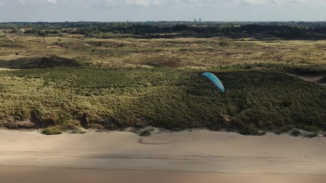 Dutch paraglider soaring and swerving along grassy coastal dune, side tracking