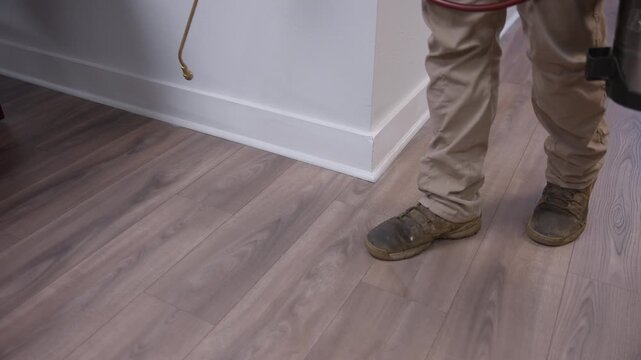 Tracking shot of pest control application being applied indoors along office baseboards and flooring.