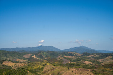 Wide panoramic view of layered green mountains under a blue sky with soft clouds. Peaceful natural landscape showing hills, valleys, and rural terrain in northern Thailand.